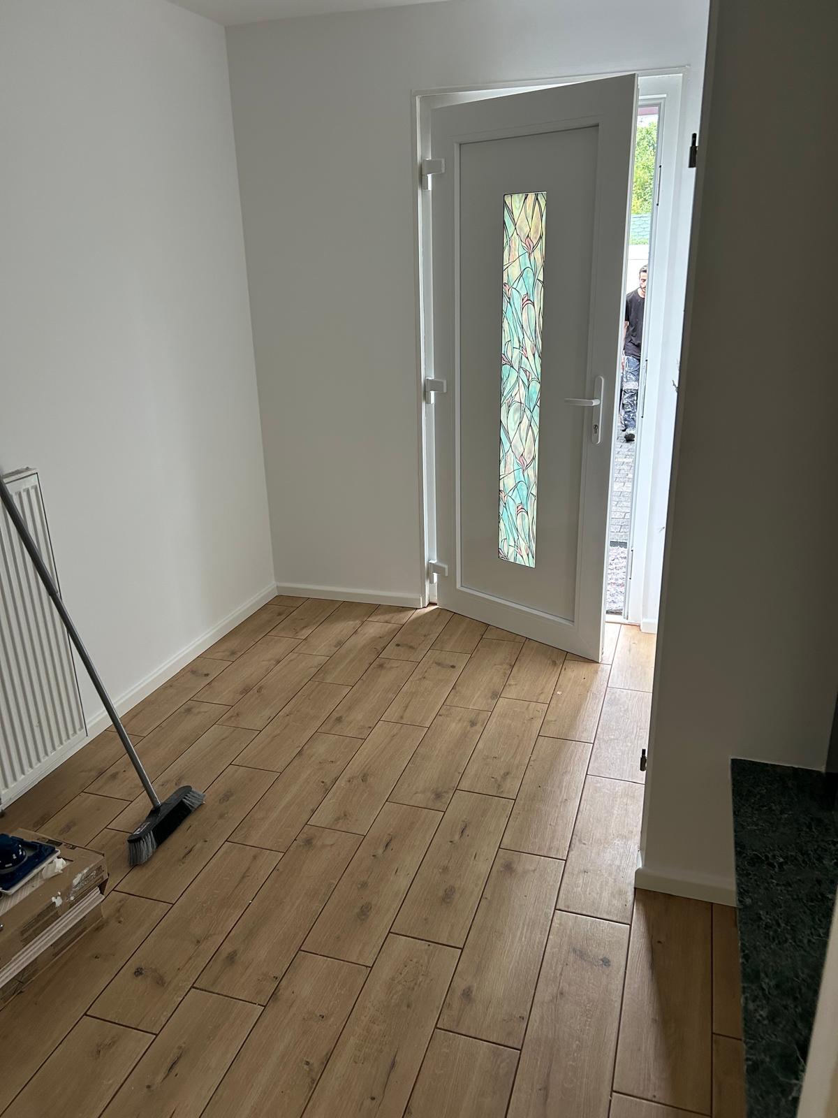 Fertig renovierter Eingangsbereich mit frisch gestrichenen weißen Wänden und neuem Bodenbelag in Holzoptik
