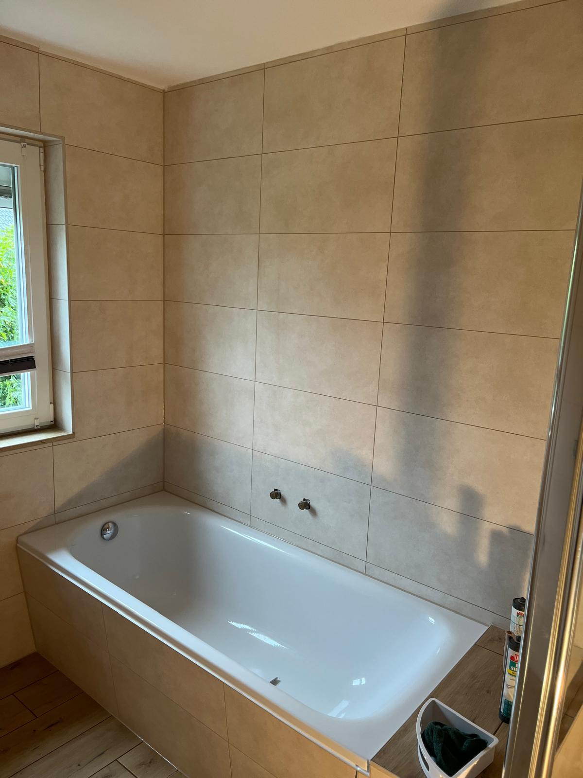 Fertig saniertes Badezimmer mit großformatigen beige-farbenen Wandfliesen und weißer Badewanne